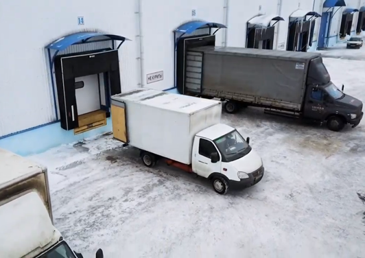 Белый и черный грузовики привезли товар на склад